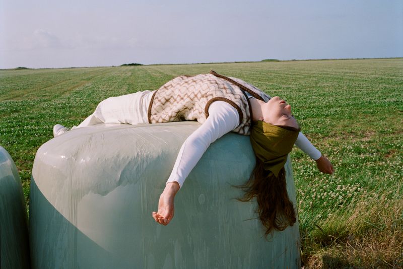 Woman in a green field laying on a haystack, arms opened