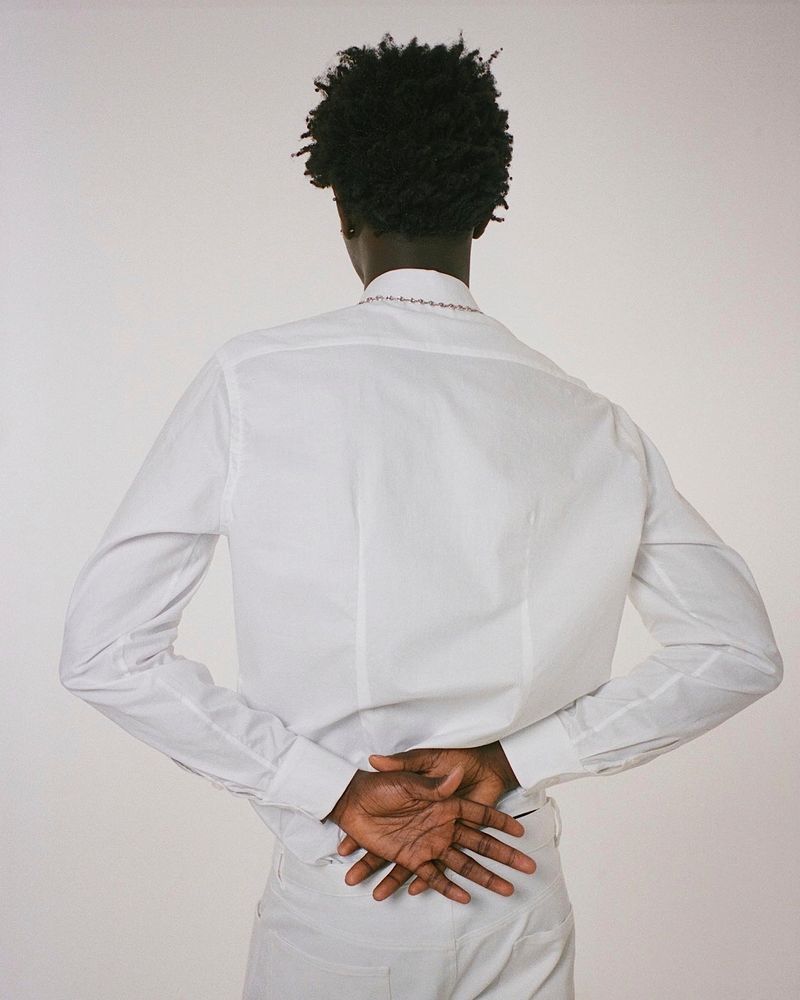 Man turned away, wearing all white, hands clasped behind his back with palms open